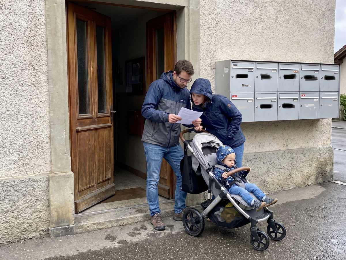Un jeune couple avec un enfant lit un document devant les boîtes aux lettres de leur immeuble